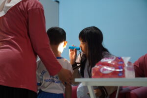 Dokter kecil tampak terampil menggunakan alat untuk memeriksa kebersihan telinga siswa