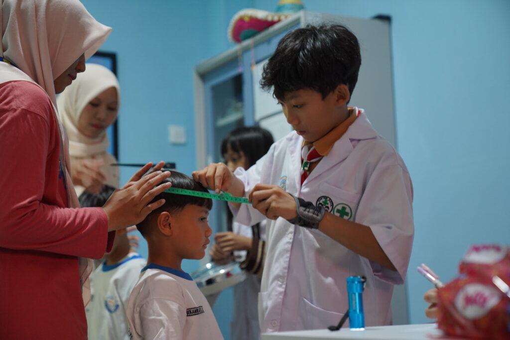 Seorang dokcil sedang membantu mengukur lingkar kepala siswa PG-K