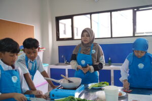Seorang teacher tampak tengah berdiri di dekat siswa, siap membantu ketika dibutuhkan