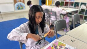 Seorang siswa tampak serius menggunting plastik untuk ditempel di gambar R. A. Kartini di hadapannya